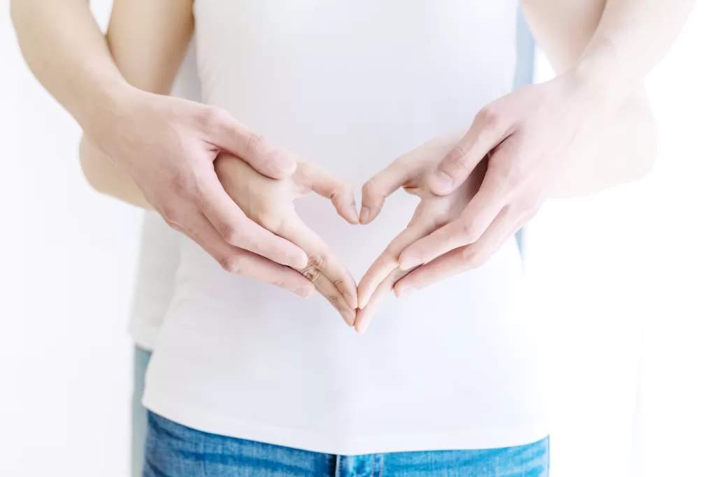 A couple forms a heart with their hands over the woman's abdomen, symbolizing nurturing fertility and hope for conception.