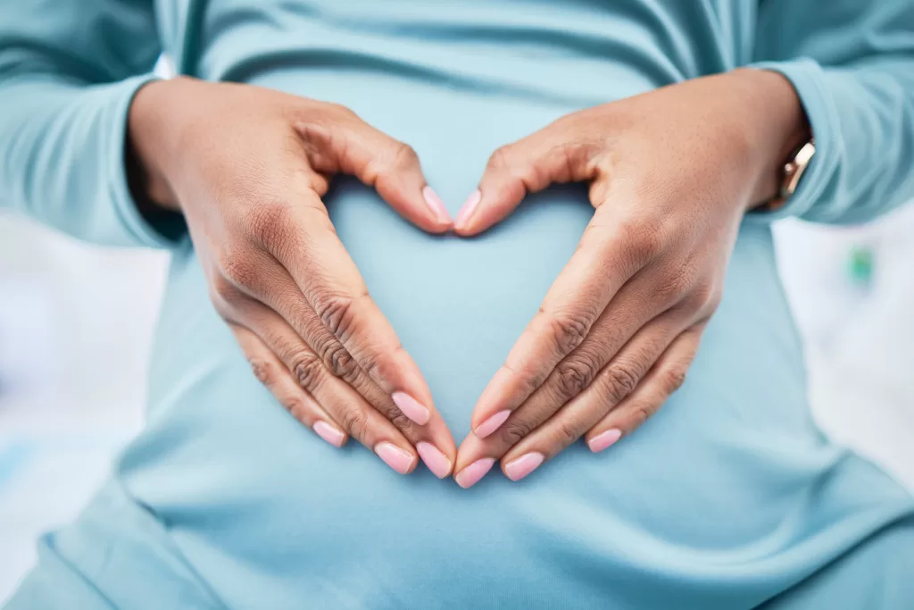 Woman forming a heart with hands over her pregnant belly, symbolizing fertility and reproductive health