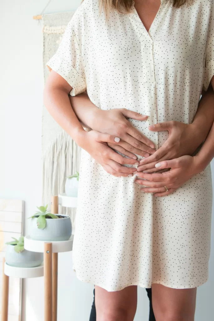 Man and woman embracing while holding her small baby bump during the first trimester of pregnancy.