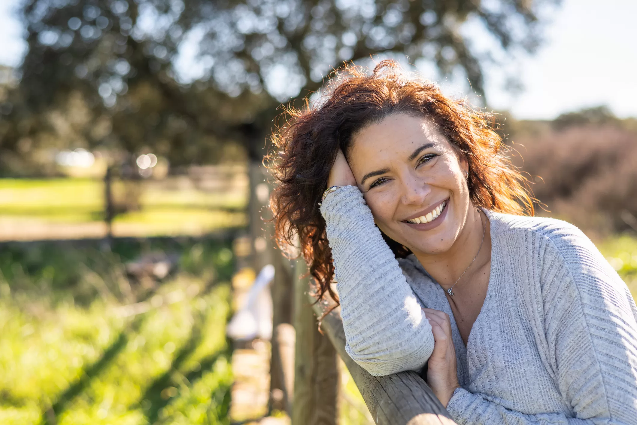 Woman smiling and leaning against a fence, representing natural hormonal and thyroid health