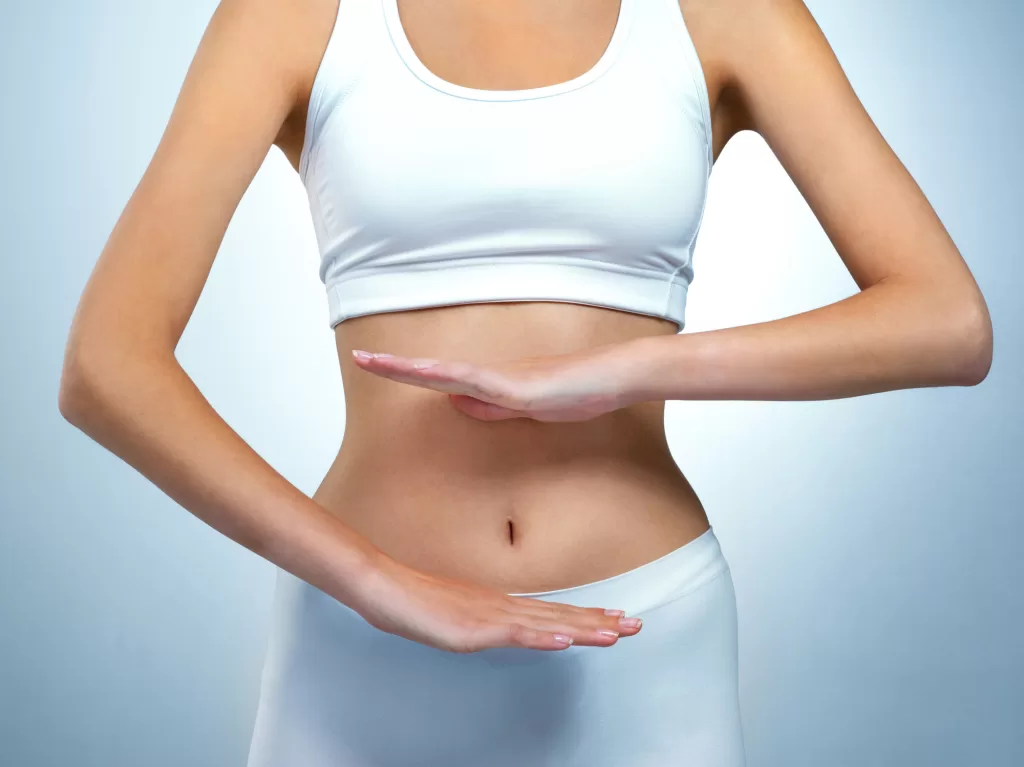 Woman holding her hands above and below her abdomen, representing weight, metabolism, and digestive health